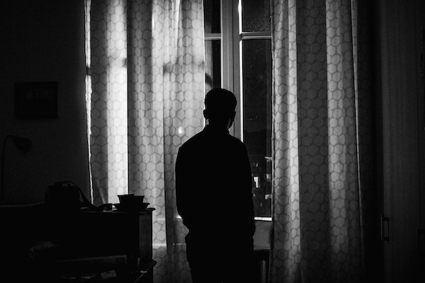 person standing by a window, looking out (black and white)