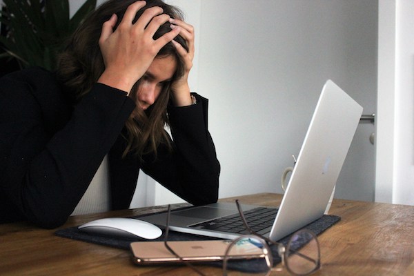 woman holding the top of her head in frustration, seated at a computer