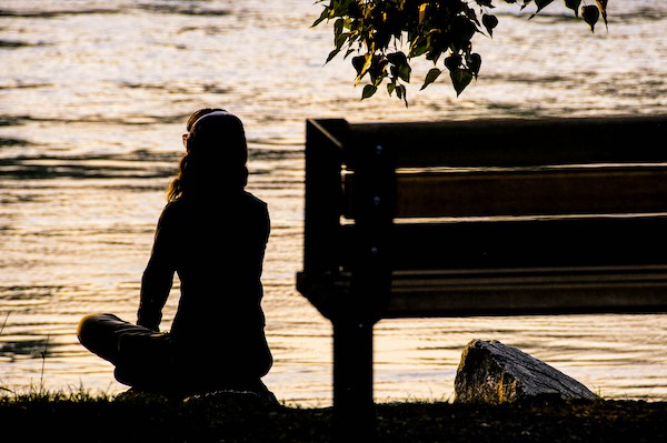 woman sitting by the water, cross-legged and next to a bench