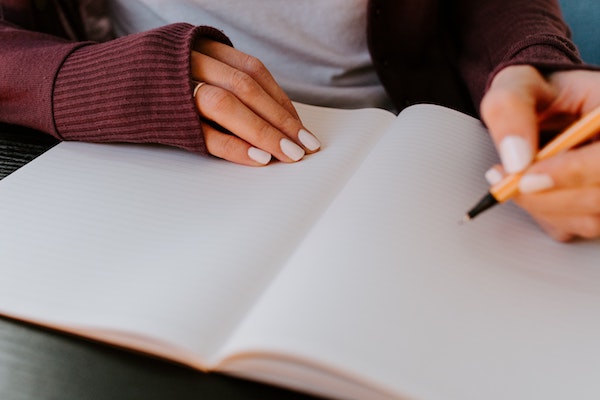 person with manicured nails writing in a journal
