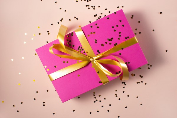 pink gift box wrapped in yellow ribbon with glitter surrounding it